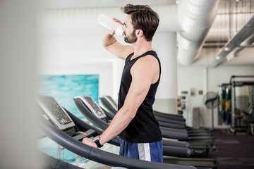 Fototapeta premium Handsome man drinking water on treadmill