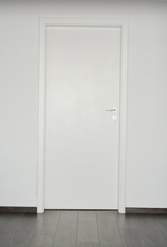 White closed door with silver doorknob on white wall background and parquet floor