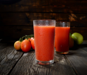Glass of tomato juice on wooden table, on wood plants background, fresh drink
