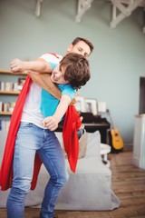 Father holding cheerful son wearing superhero costume