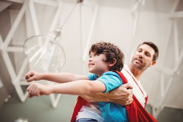 Low angle view of father holding cheerful son wearing superhero 