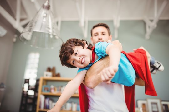 Portrait of father carrying son wearing superhero costume