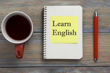 Learn English Text written on notebook page, red pencil and coffee cup. Office desk table top view