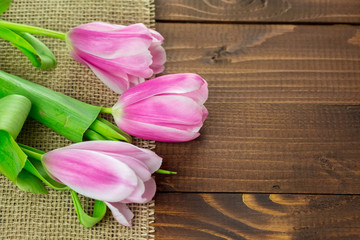 beautiful pink tulips lying on the burlap on the background of old brown boards. The idea of Mother's day cards, March 8, birthday with free space for your text