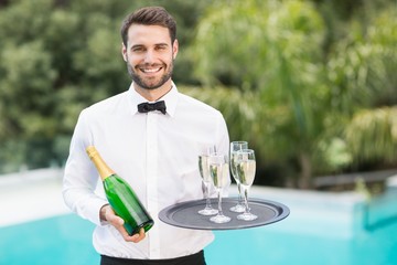 Smiling waiter holding champagne flutes and bottle