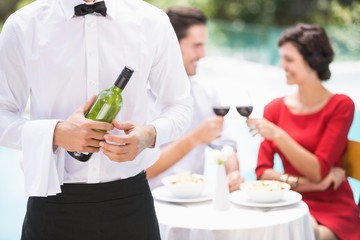 Midsection of waiter holding wine bottle 