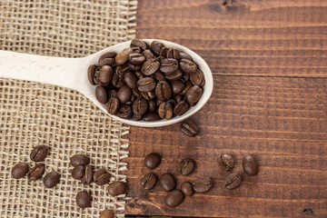 whole coffee beans in a wooden spoon and a scattering of coffee beans on burlap and old brown boards with free space for your text