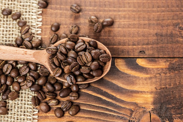 whole coffee beans in a wooden spoon and a scattering of coffee beans on burlap and old brown boards with free space for your text