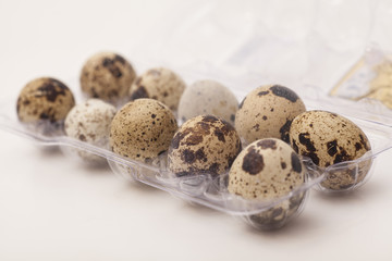Obraz premium Quail eggs in transparent plastic container on white background