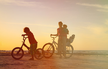 Fototapeta na wymiar happy mother with two kids biking at sunset