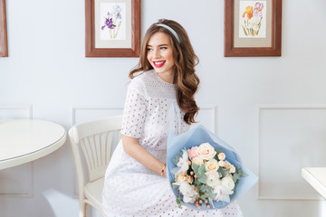 Happy lovely woman with bouquet of flowers sitting in cafe