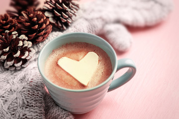 Cup of hot cappuccino with heart marshmallow, warm mittens and pine cones on pink background