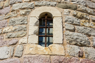 Fototapeta na wymiar Ancient window with cell in the stone wall.