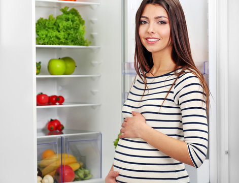 Pregnant woman standing near open fridge in the kitchen