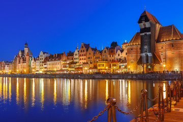 Fototapeta premium Old harbour crane and city gate Zuraw in old town of Gdansk, Dlugie Pobrzeze and Motlawa River at night, Poland