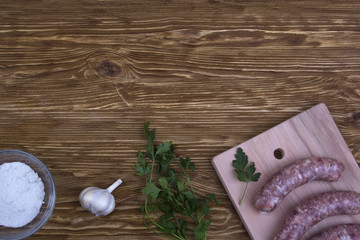 Raw sausages, salt and garlic on wooden table