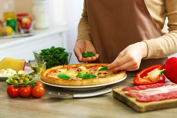 Woman decorating fresh baked pizza with basil, close up