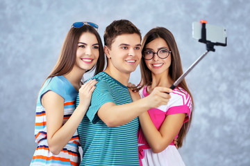 Teenager friends making photo by their self with mobile phone on grey background on grey background