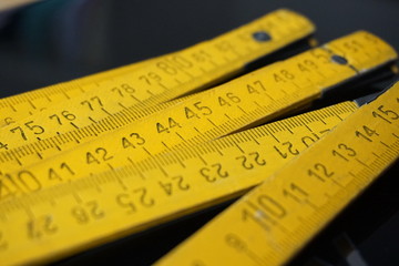 Old yellow folding meter ruler measuring centimeters on the black surface - Powered by Adobe