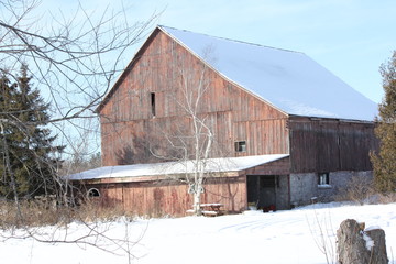 Large, old, faded barn with snow covering the roof and ground. 