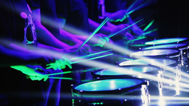 A group of people synchronously hit the percussion in the rays of light.