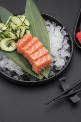 Salmon sashimi on a bamboo list and ice over black background