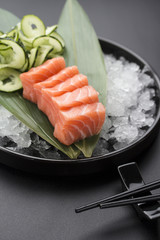 Salmon sashimi on a bamboo list and ice over black background