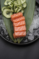 Salmon sashimi on a bamboo list and ice over black background