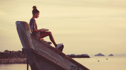 Young woman is sitting on the shipwreck and reading a book.