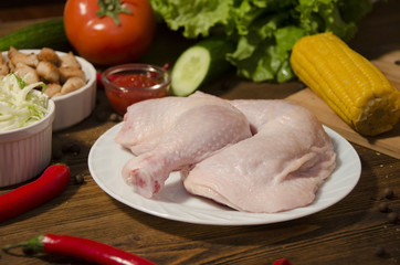 raw chicken legs on wooden background with vegetables and pepper