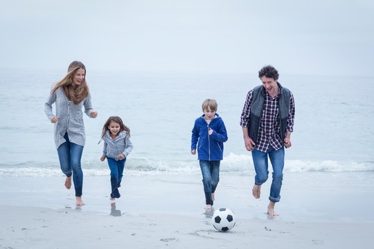 Cheerful family playing soccer at sea shore against sky