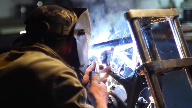 Automaster weld the frame of a custom motorcycle in the garage. Sparks welding machine. Protective face mask.