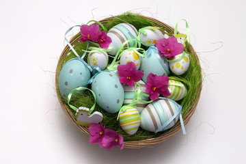 Decorated Easter eggs with pink flowers in a shallow basket, isolated on white background