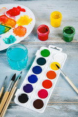 Naklejka premium Set of watercolor paints, brushes for painting and palette on old vintage wooden background top view