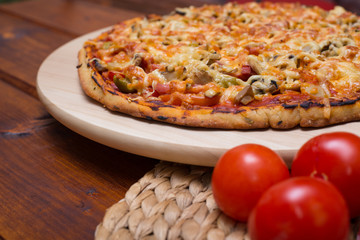 Italian pizza with ham and mushrooms on a wooden board on a background of tomato on wooden table