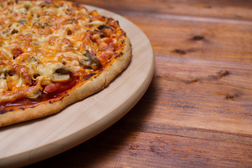 Italian pizza with ham and mushrooms on a wooden board on natural wooden table
