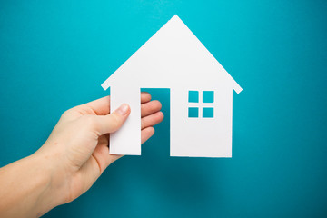 Fototapeta na wymiar Hand holding white paper house figure on blue background. Real Estate Concept. Ecological building. Copy space top view.