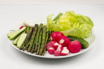 Food arrangement with fresh red radishes, cucumbers, lettuce and grilled asparagus on a white plate