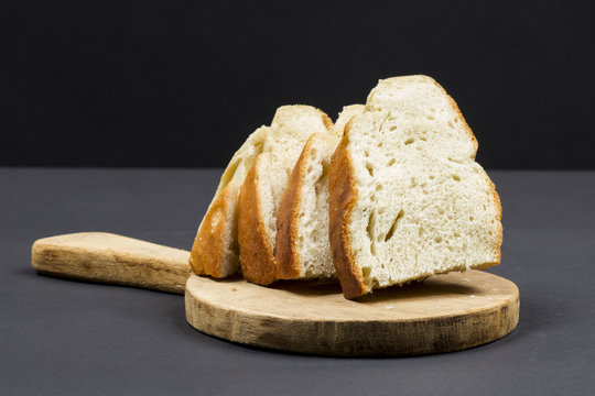 Still life composition with wooden kitchen cutting board and bread on dark background