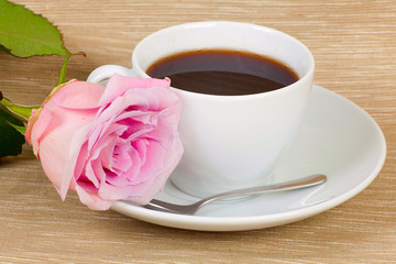 White cup of tea on the wooden kitchen table with red rose