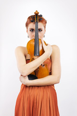 Young red-haired girl with a violin in her hands on a white background.evening dress.Long orange...