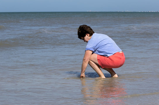 Woman walking on beach collecting seashells - Powered by Adobe