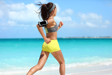Fit woman cardio training doing running workout on beach. Unrecognizable athlete runner jogging fast on summer ocean background wearing a phone armband holder for music listening on smartphone app.