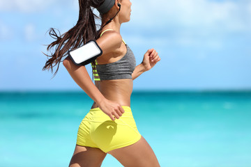 Sports phone armband fitness jogger exercising on beach - cardio workout. Midsection closeup of...