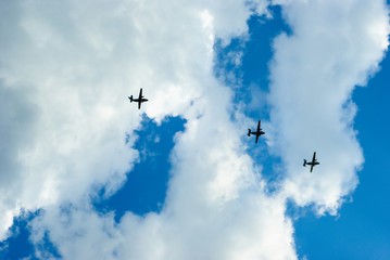 Three aircraft are flying in the sky with clouds