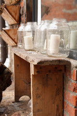 White big candles in glass jars on a narrow retro wooden table outdoors. Simple creative ideas for home and country house. Decorations for windows at Christmas.