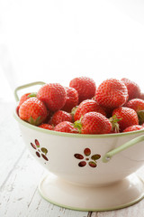 Fresh strawberries in a colander with light coming from behind.