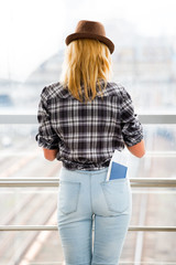 young woman in a hat and turned his back is against the background of glass wall. pocket a passport and a ticket