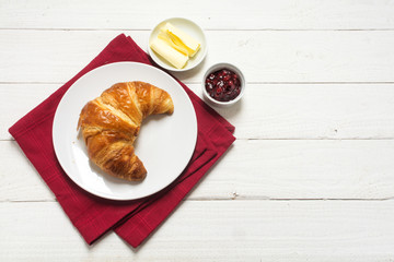 breakfast with croissant and jam on a red napkin on white wood