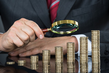 Close-up Of Businessman Examining Coins With Magnifier